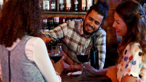 Barman-serving-red-wine-female-customers-at-bar-counter
