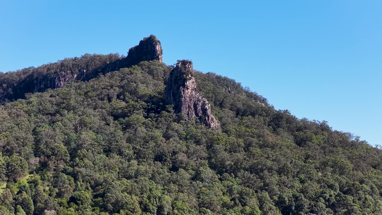 Drone footage captures Nimbin Rocks' rhyolite formations surrounded by lush eucalyptus forest under clear blue skies
