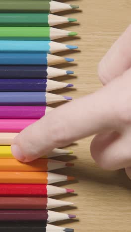 vertical video of coloured pencils arranged in a line on wooden background with person choosing yellow one