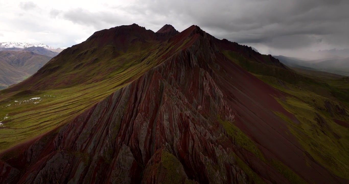 Creste aspre della Montagna Arcobaleno Pallay Punchu sotto nuvole drammatiche in Perù, approccio aereo con drone con pendii illuminati dal sole e scogliere erose a drappeggio.