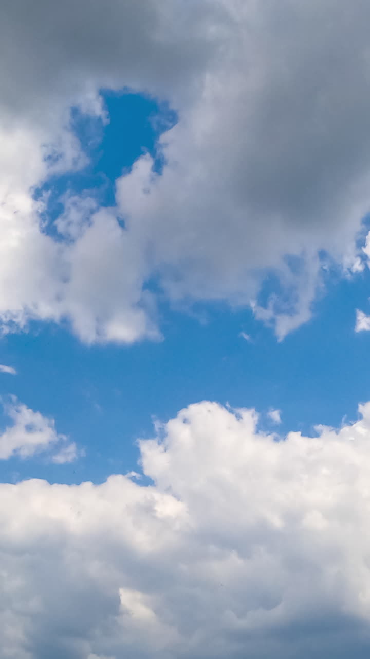 Soft light white clouds quickly floating by the azure skies. Soft clouds gathering into a big cloudscape. Low angle view timelapse. Vertical video