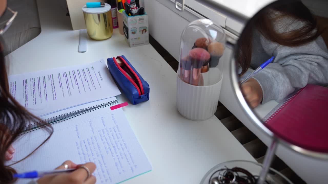 fotografía en primer plano de un escritorio de estudio con materiales de escritura y pinceles de maquillaje mientras las manos de la mujer escriben