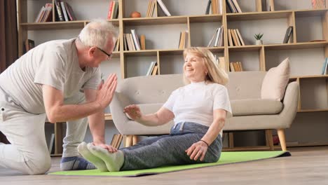senior couple doing sports at home husband helping wife to do exercises senior couple doing sports at home husband helping wife to do exercises a happy couple spends time together in two