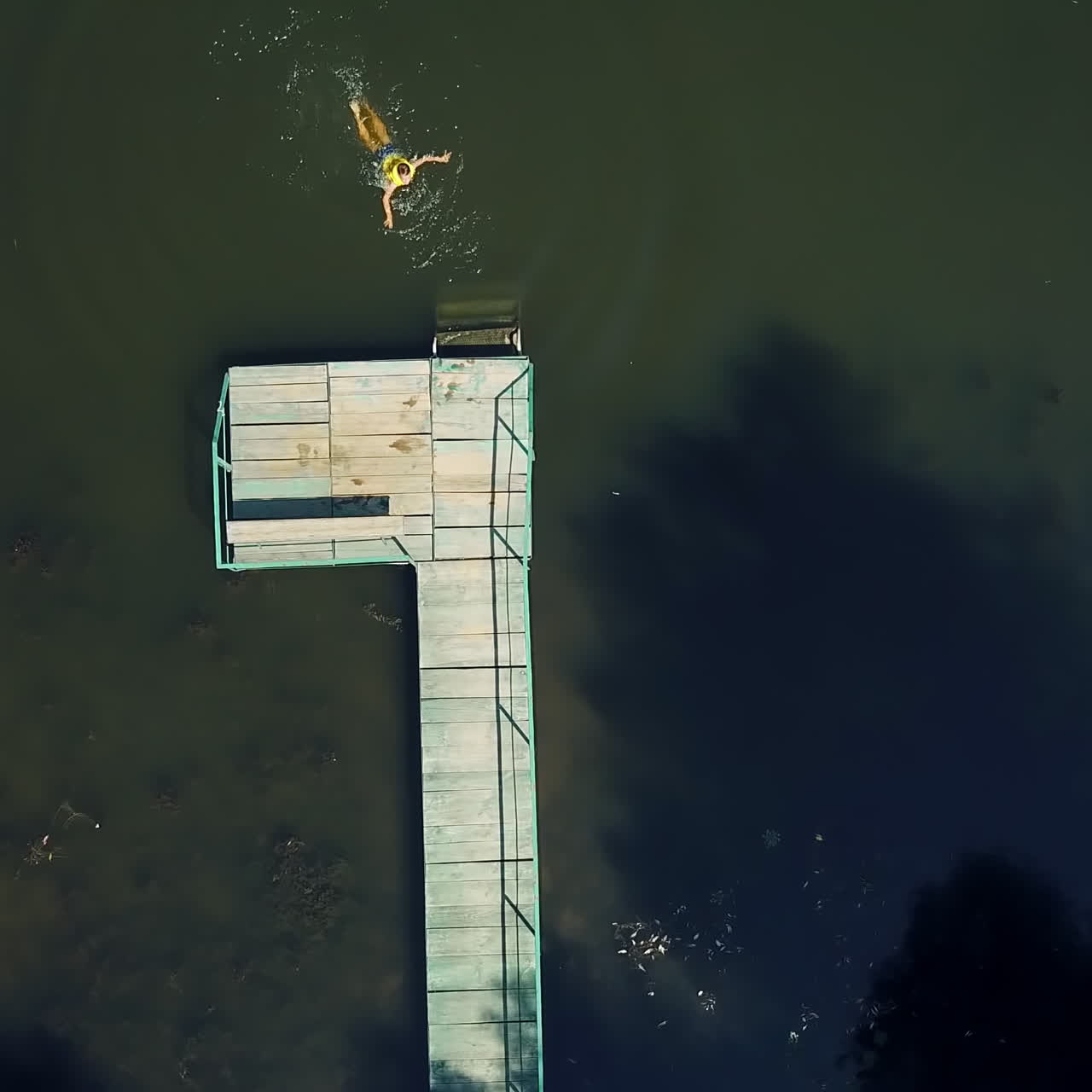 Top view of an active boy going into the edge of the bridge and jumping into the water. Little kid enjoys jumping and swimming in the river outdoors. Aerial view