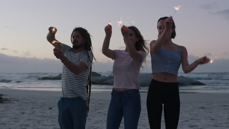 cheerful group of friends celebrating on beach waving sparklers at sunset