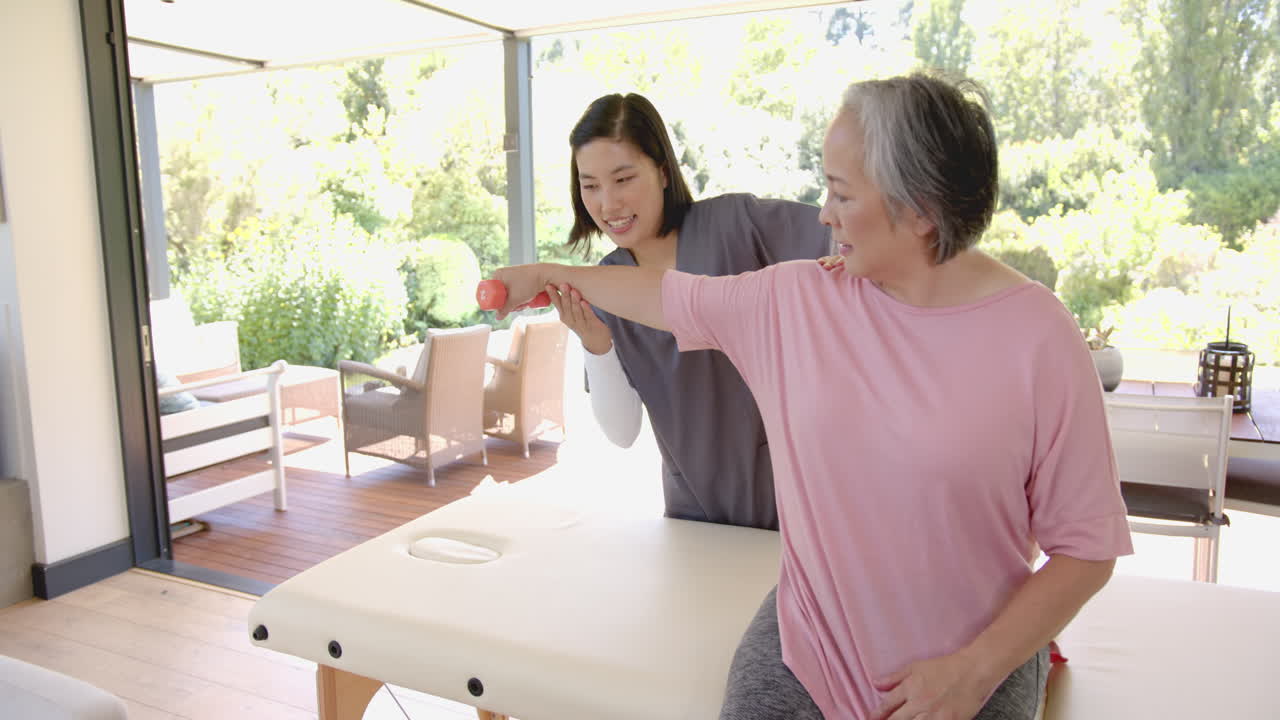 Senior asian woman receiving physical therapy, therapist assisting with arm exercise
