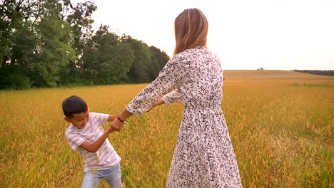 lovely asian mother spinning with her little fellow on wheat field