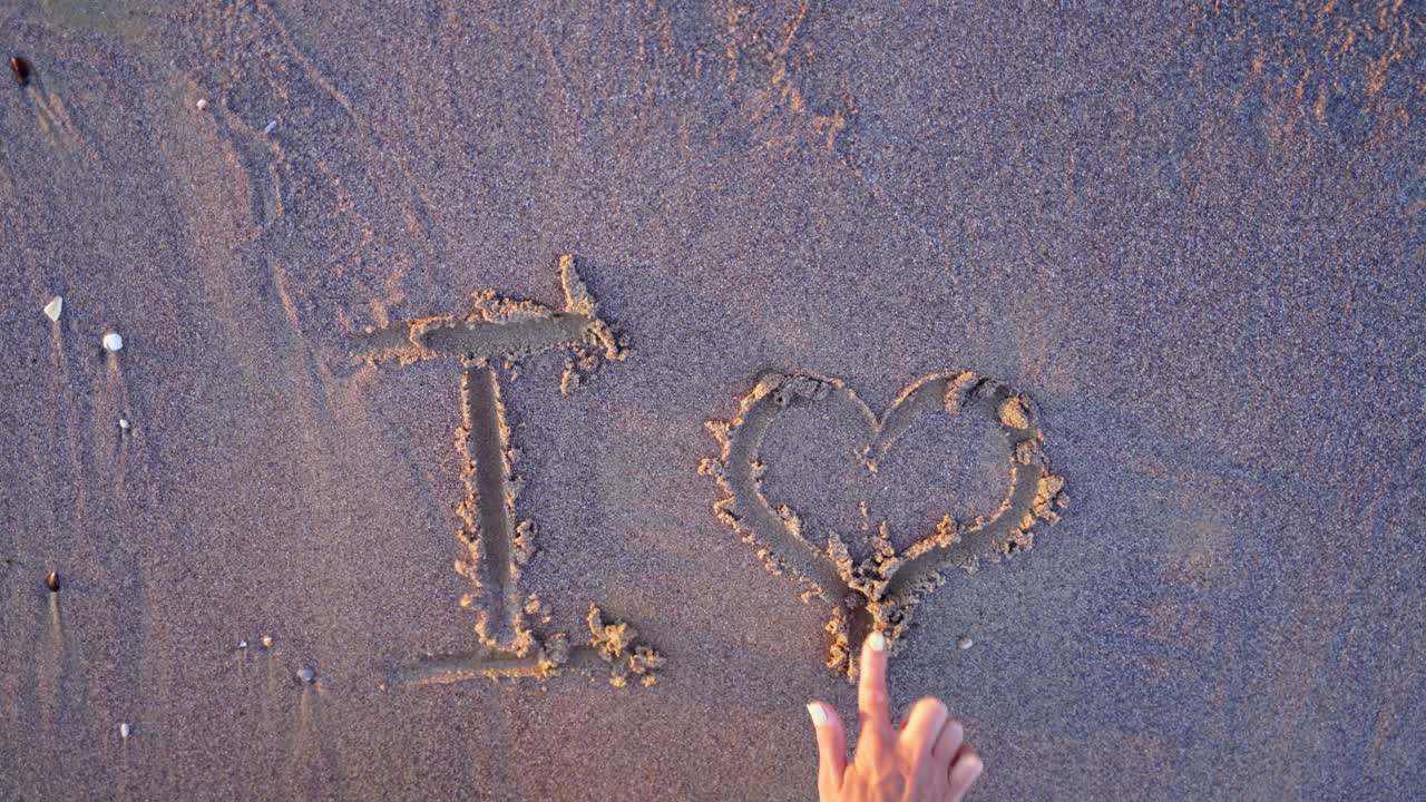 Girl painting on the sea sand. Young female is writing on a sandy beach in the evening. Top view. Close-up.