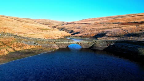 Imágenes-De-Video-Aéreas-De-Un-Pequeño-Puente-Construido-En-Piedra-Que-Cruza-Un-Embalse-Y-Un-Río-En-Lo-Alto-De-Las-Colinas-Peninas,-Al-Oeste-De-Yorkshire,-Inglaterra