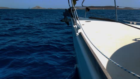 vista de un mar muy azul y ondulado y colinas en el horizonte desde un yate blanco navegando tranquilamente en un día soleado de verano en un país del sur de europa
