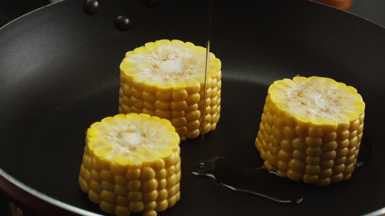 Pouring Oil Over Fresh Corn on the Cob in a Frying Pan