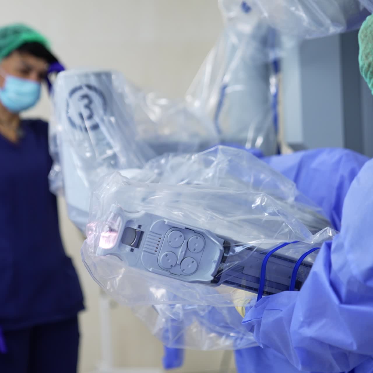 Female medic dealing with the equipment coated in plastic in surgery room. Colleague standing at backdrop in blur rushing to help