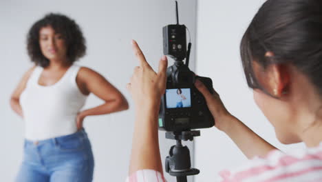 female photographer in digital studio shooting images on camera tethered to laptop computer