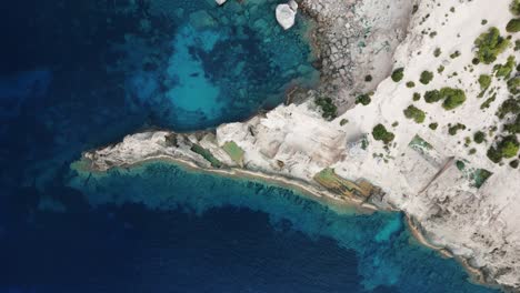 the drone is flying topdown above a small rocky coast with the clear blue sea in ibiza spain aerial footage 4k