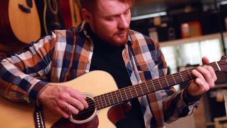 irlandés pelirrojo barbudo hombre guapo en camisa casual a cuadros marrón eligiendo una guitarra en una tienda de música
