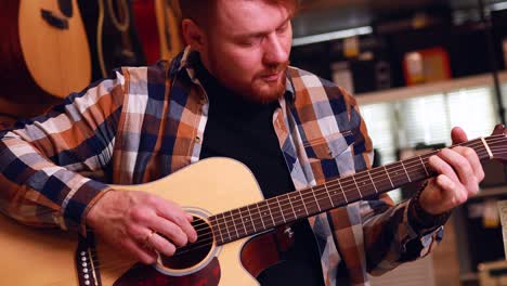 irishman redhaired bearded handsome man in brown plaid casual shirt choosing a guitar in a music store