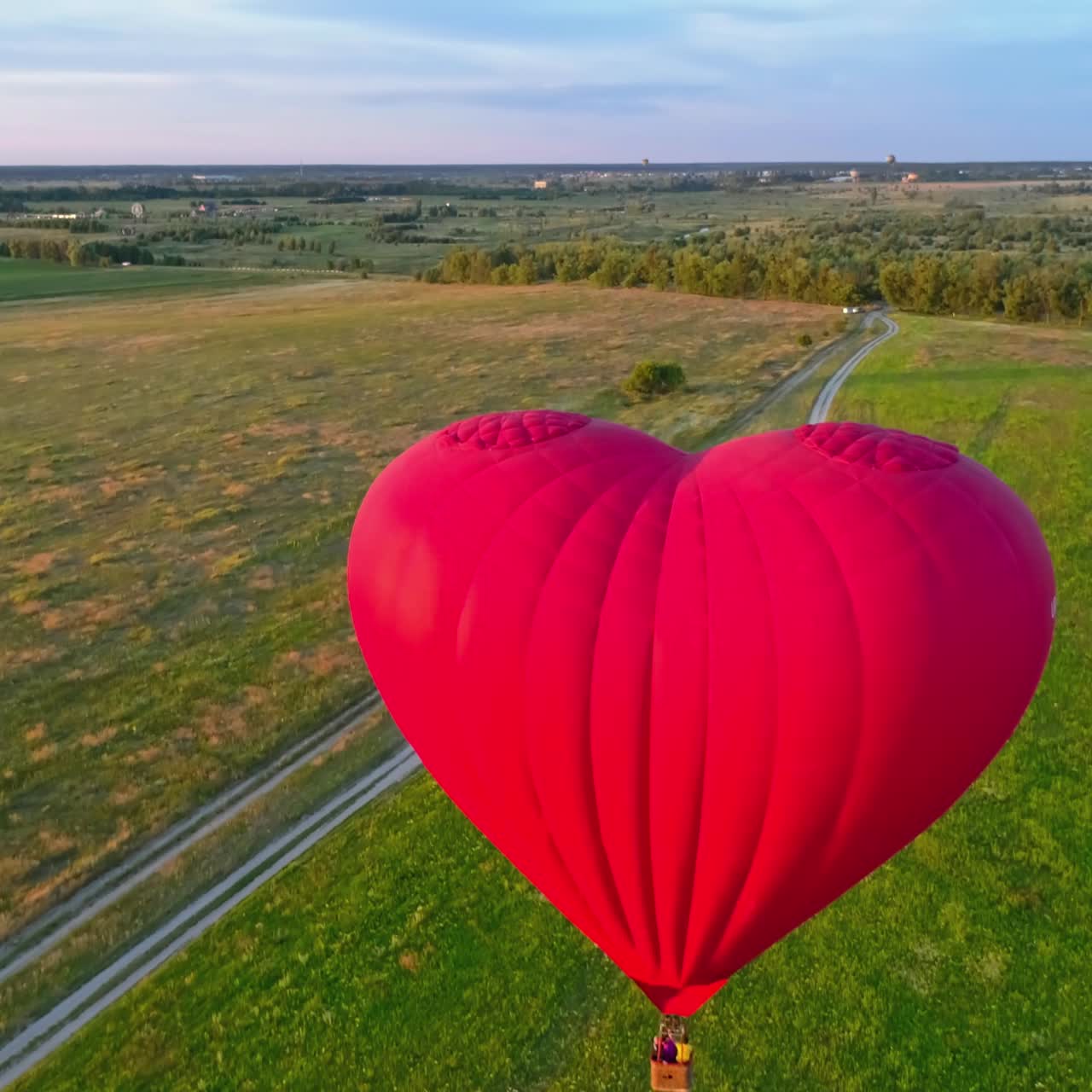 Large aerostat in the air. Beautiful red hot air balloon in the heart shape flying in the countryside. People travel in the basket of the airship in summer. Close-up.