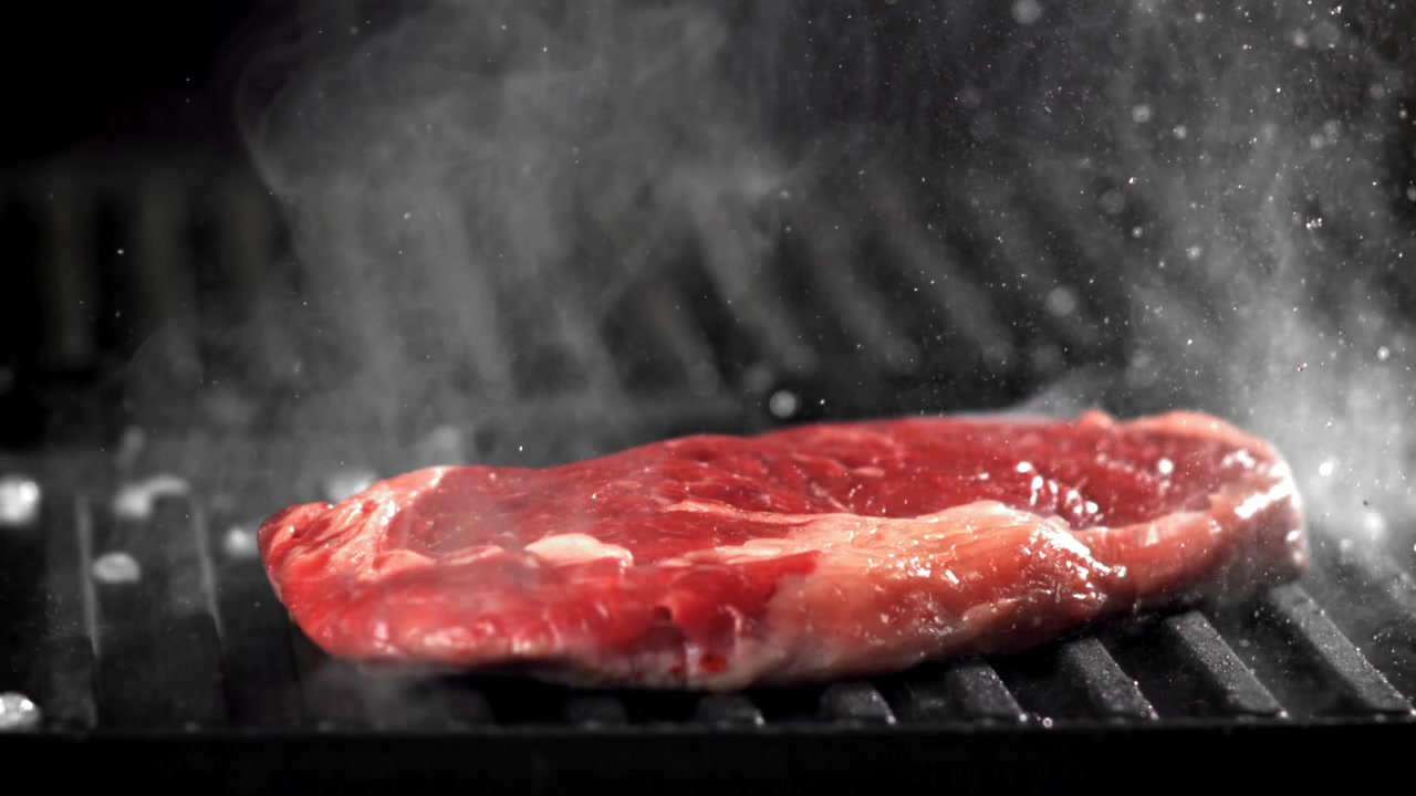 Raw Beef Steak Sizzling and Steaming on a Hot Grill