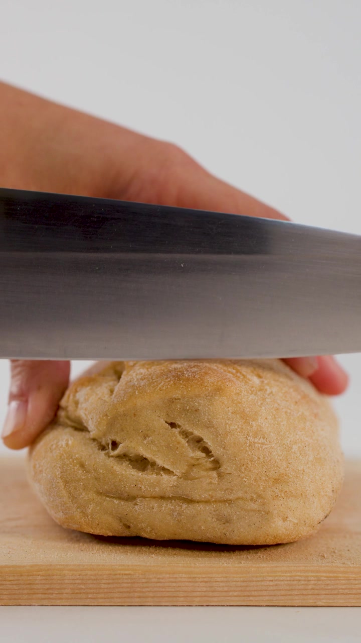 Close-up of hands slicing a fresh bread roll with a chef knife on wood.