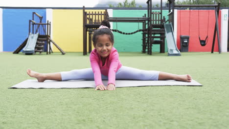 in a school playground, a young african american girl is doing a split