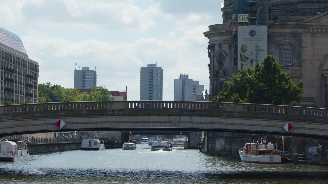 Tour boats travel beneath city bridge on Spree River, Berlin, during bright summer daylight