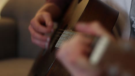 a young man is playing guitar, the focus racks from chord hand to strumming hand and back again