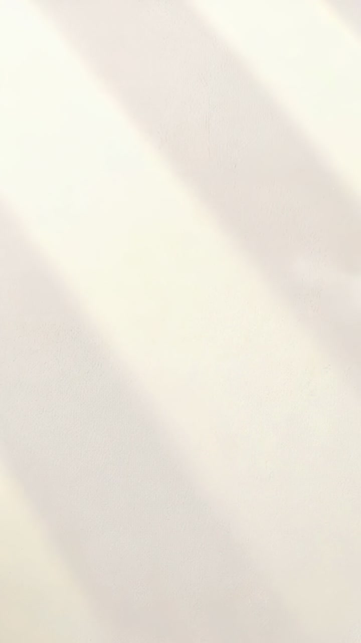 Video verticale: Luce solare mutevole che proietta ombre diagonali su una parete color crema all'interno di una stanza mentre il sole si sposta