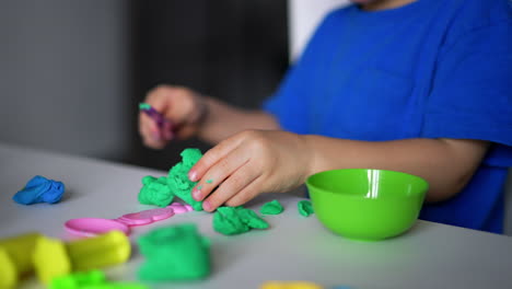 unrecognized toddler using a stick to cut the plasticine into pieces. little child playing at home. close up.