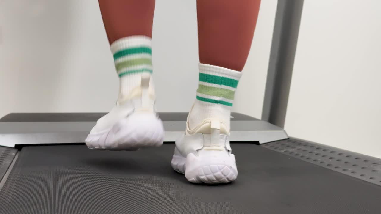 A person walks on a treadmill in a home gym, captured in slow motion. Bright lighting highlights the rhythmic movement of feet
