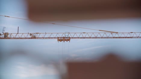 detail of the arm of a yellow construction crane in motion seen through out of focus foreground objects