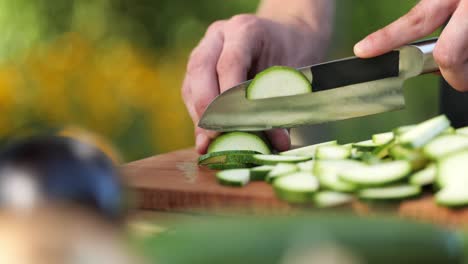 young man cutting zucchini on a wooden board in his garden close up