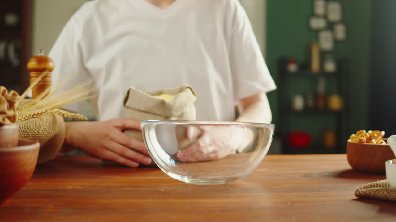 Person Pouring Cornmeal into a Glass Bowl in a Kitchen