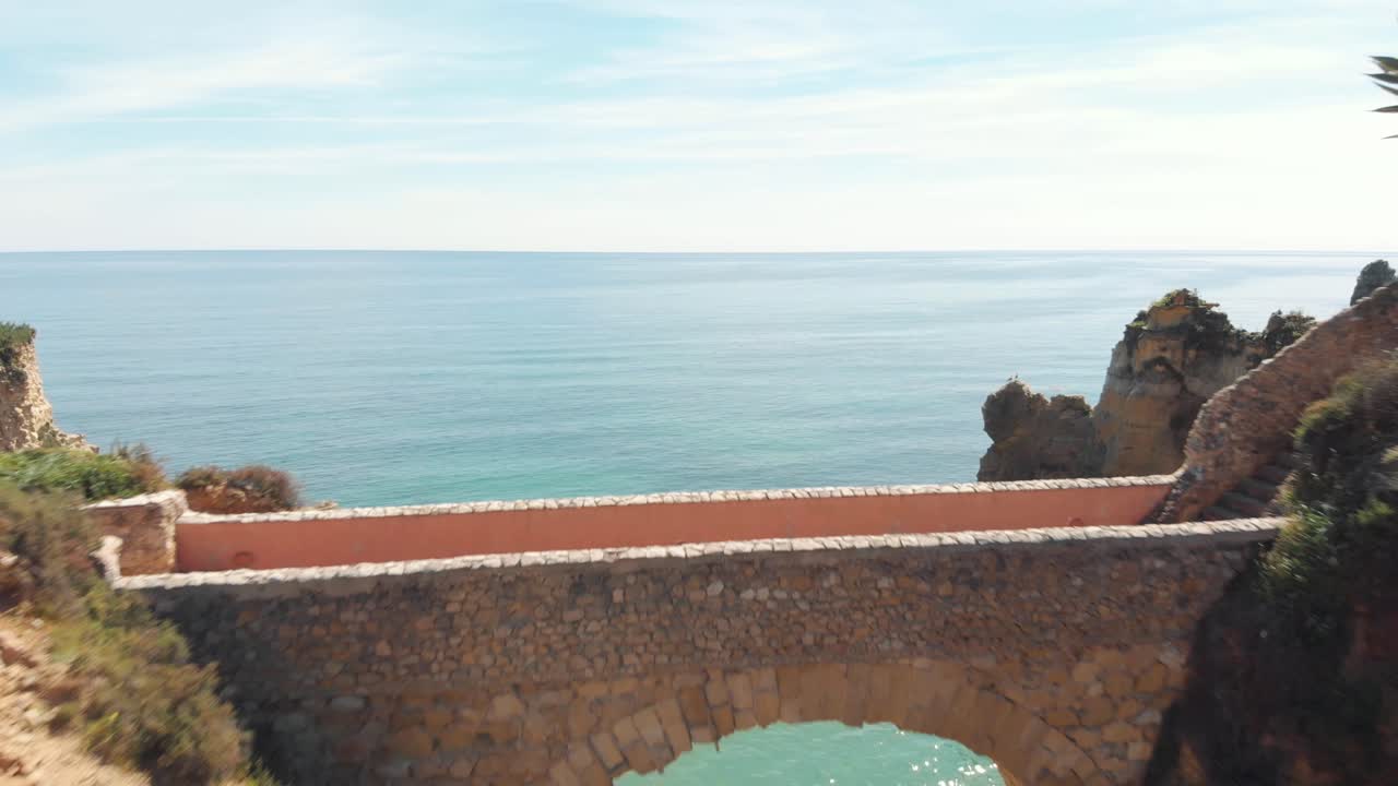 римский мост на пляже эстуданте, соединяющий размытые скалы в лагосе, алгарве, португалия - съемка с воздуха с пролетом в кадре