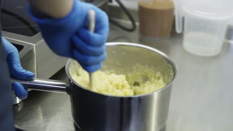 Process-of-creating-brewed-dough-for-eclairs-or-profiteroles.-Confectioners-hands-in-blue-gloves-mix-all-ingredients-together-in-a-cooking-pan-to-create-delicious-brewed-dough.