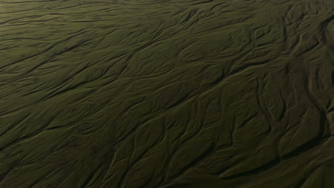 Flying-over-glacier-river-braids-Iceland,-pan-up-to-reveal-glacier