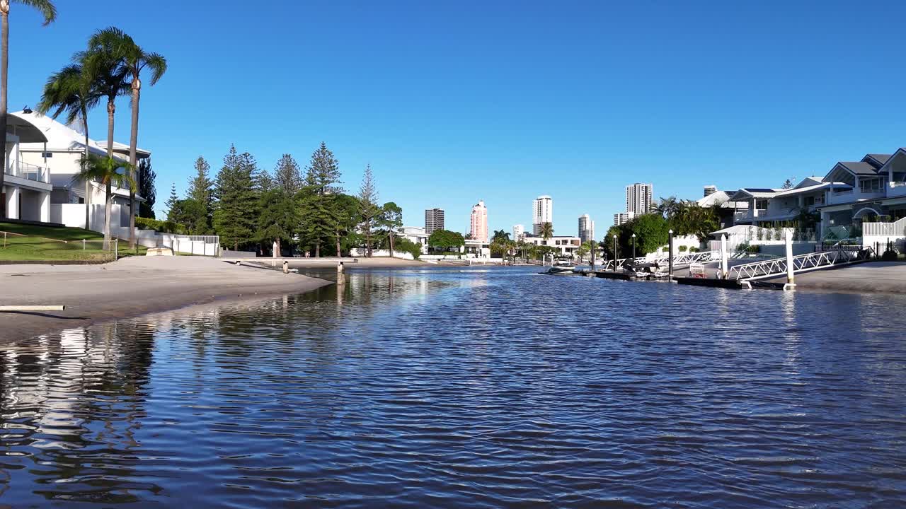 Drone captures tranquil river and modern houses under clear blue skies in Gold Coast, Australia. Calm water reflects vibrant surroundings