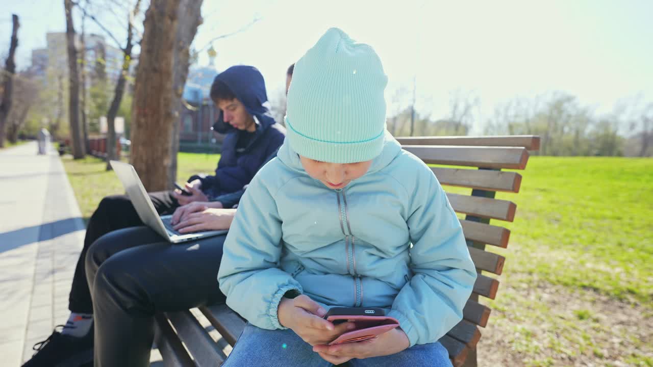 Młoda dziewczyna korzysta ze smartfona, siedząc na ławce w parku