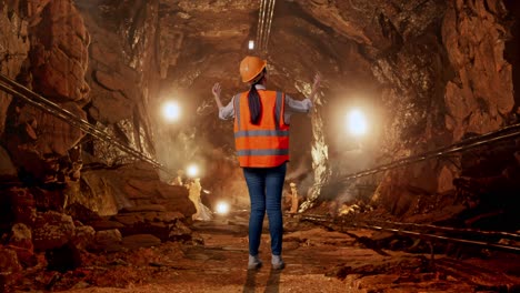 full body back view of a female engineer with safety helmet spreading arms in underground mine tunnel