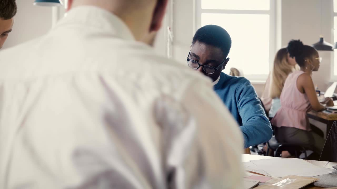 concentrado joven afroamericano trabajando duro en el boceto de arquitectura con colegas en el espacio de oficina de moda 4k