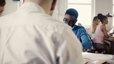 concentrated african american young man working hard on architecture sketch with colleagues in trendy office space 4k
