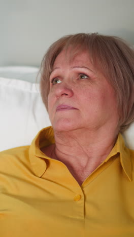 worried elderly woman lying in bed in hospital feeling sick. nurse gives female patient medicine and water. care in modern medical facility closeup