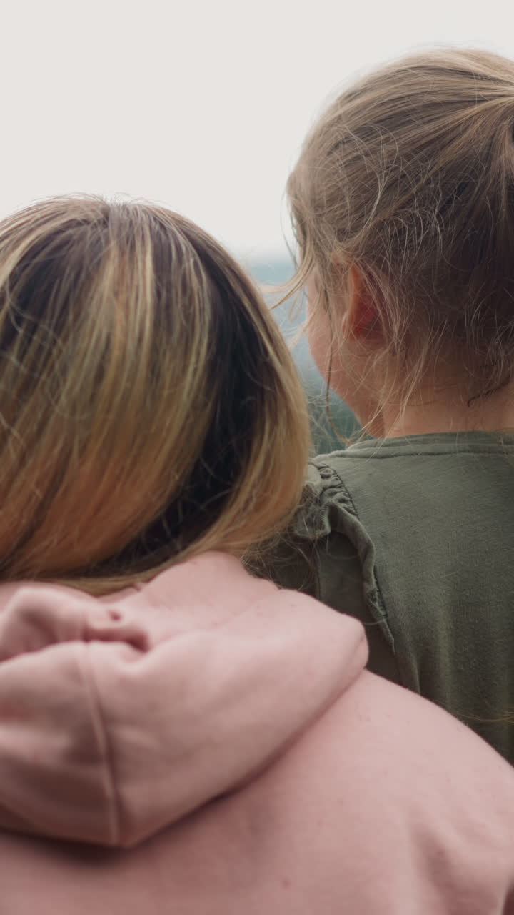 Family of mother and little children rests enjoying view of distant mountains covered with wild forest in mist on cloudy day backside view