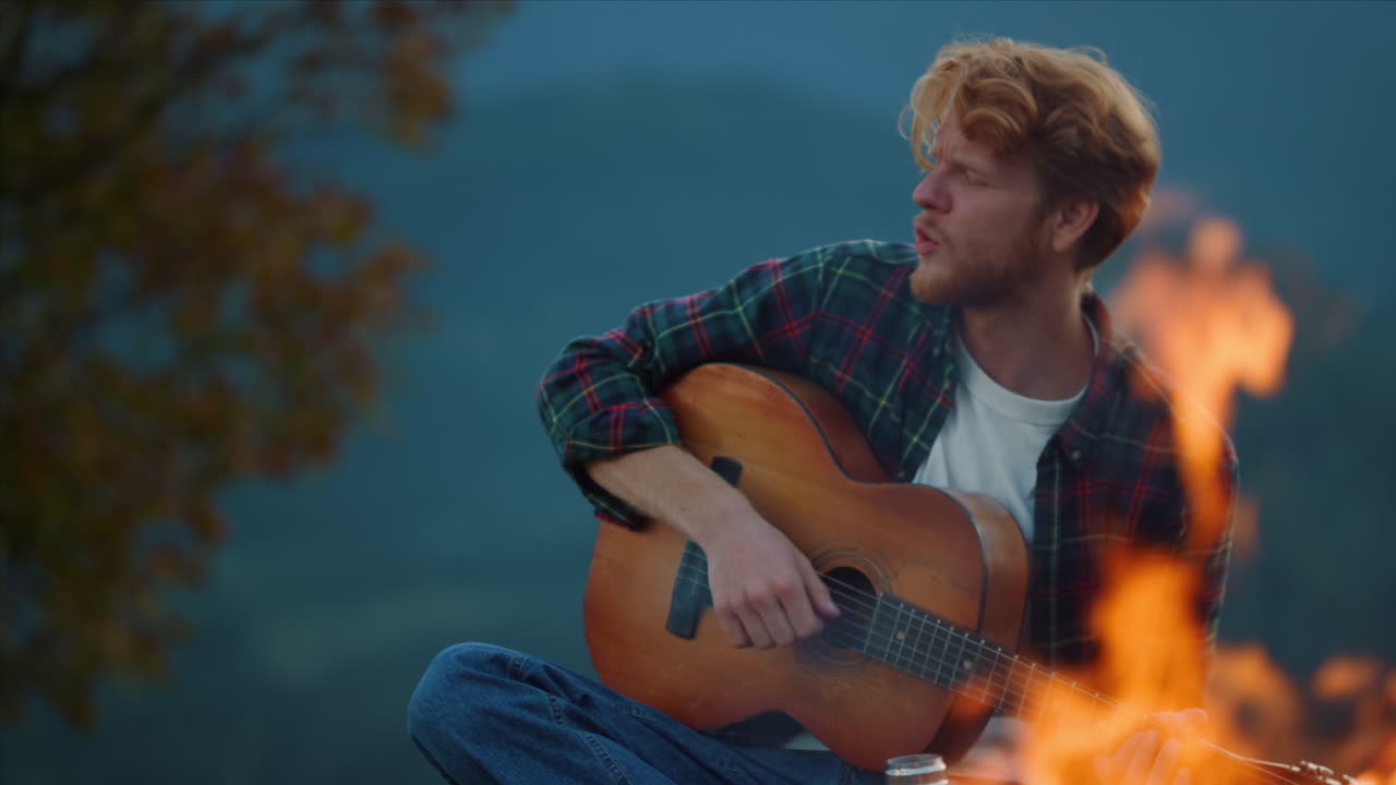 Ung guitarist spiller musik i aftenens natur. Nærbillede af fyr, der nyder at spille guitar i skoven.