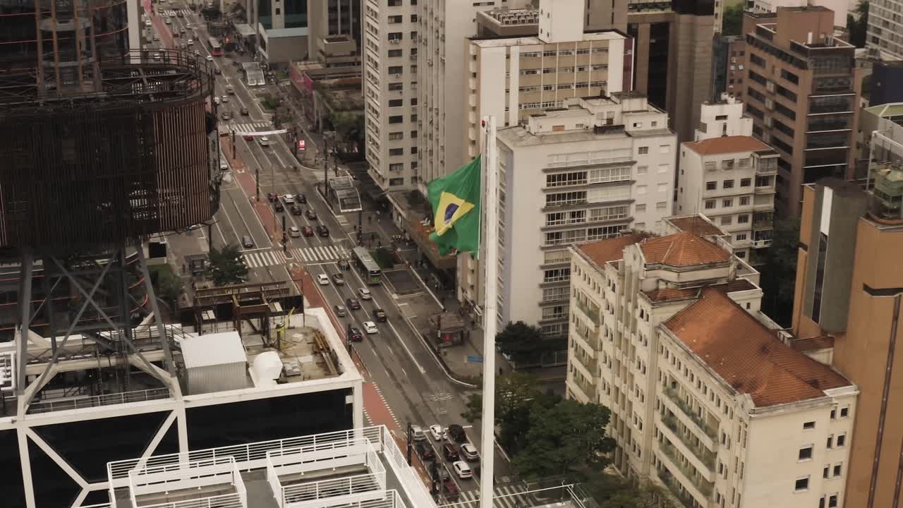 Bandeira Brasileira tremulando ao vento sobre edifícios arranha-céus da cidade de São Paulo, vista de baixo para cima.