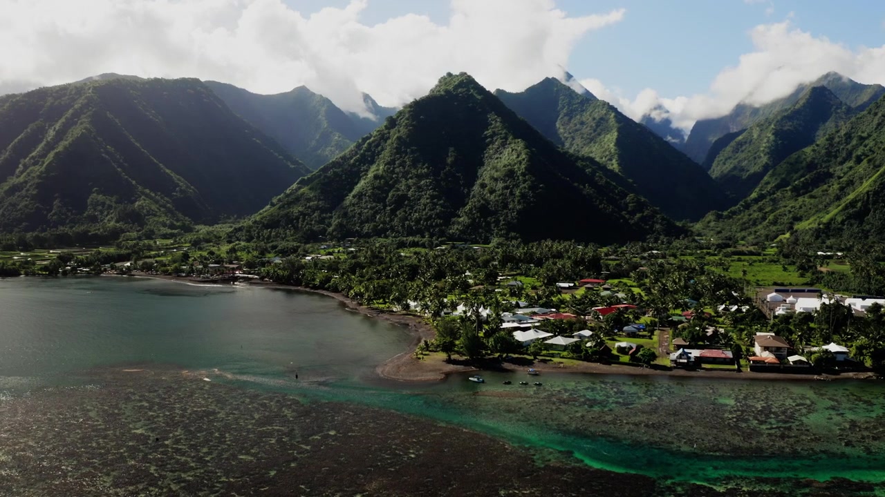 Tahiti'deki Teahupoo köyünün üzerinde sisin içinden süzülen drone, sırt hattındaki alçak bulutların altında sakin bir lagüne bakan kıyı evleri.