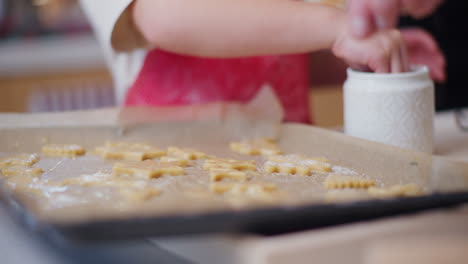 close-up of boy's hand who sprinkles sugar on cookies