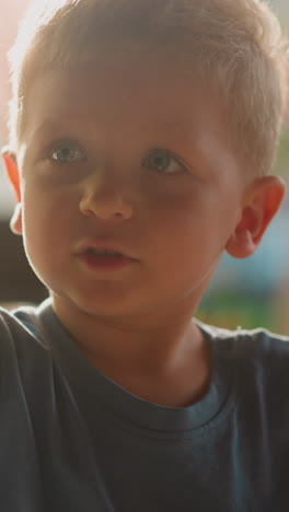 cute little boy plays with empty glass as listening tool sitting in room lit by bright sunlight at home extreme close view slow motion