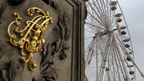 ferris wheel spinning on a cloudy day with a gold sign of a stature in front of it