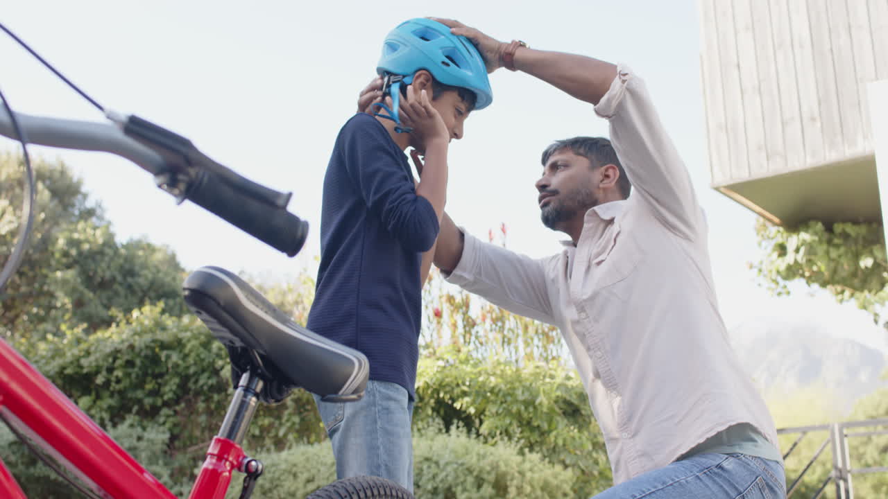 Indian father helping young son adjust helmet while preparing to ride bicycle