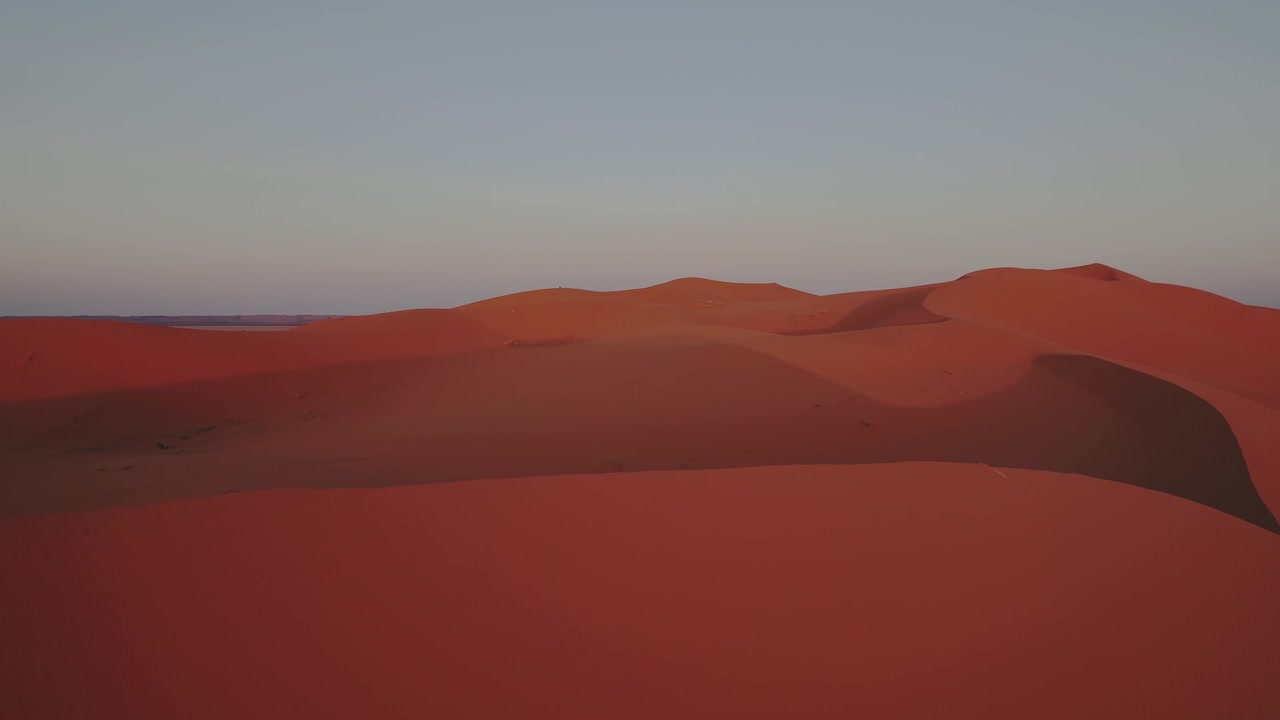 L'imponente duna di Erg Chebbi si erge sopra il Sahara vicino a Merzouga, Errachidia, Drâa-Tafilalet, Marocco, Africa, risplendendo con i caldi toni del tramonto, ripresa con drone in scivolata laterale e imbardata